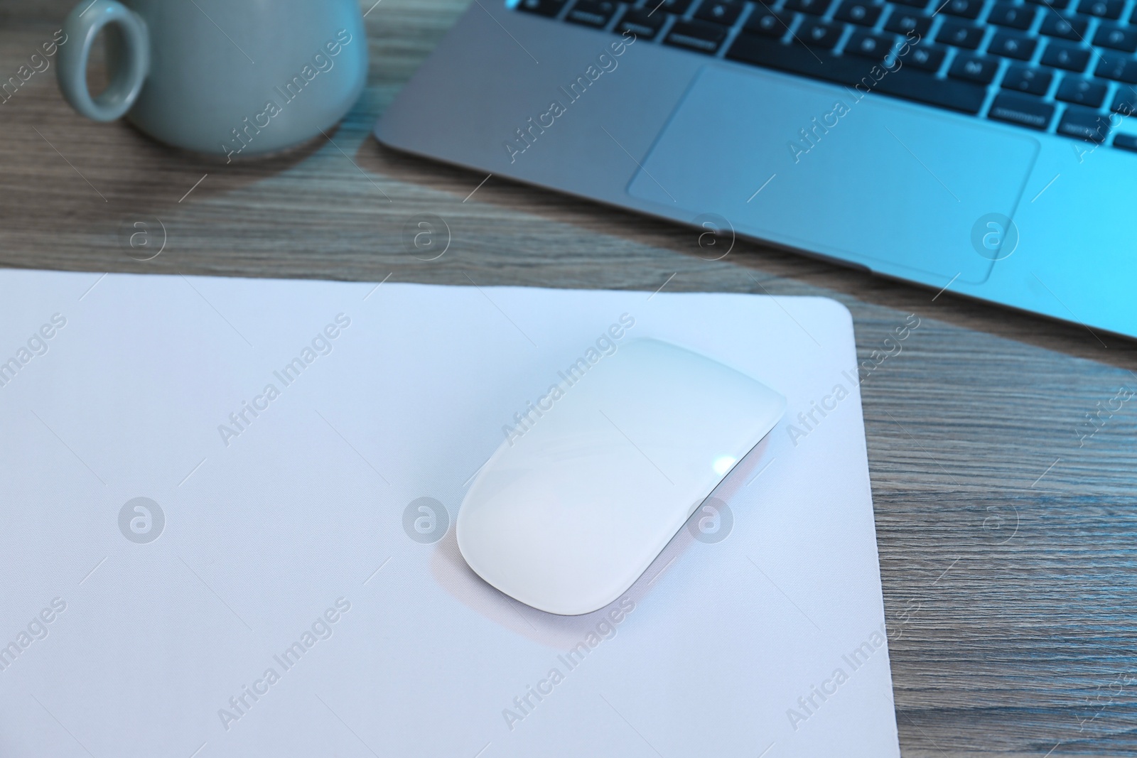 Photo of Computer mouse with mousepad and laptop on wooden table