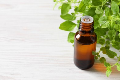 Photo of Essential oil in bottle and oregano leaves on white wooden table, closeup. Space for text