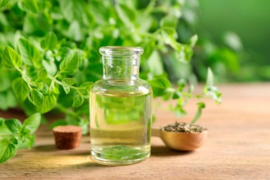 Photo of Essential oil in bottle, spoon with dry herb and oregano twigs on wooden table, closeup