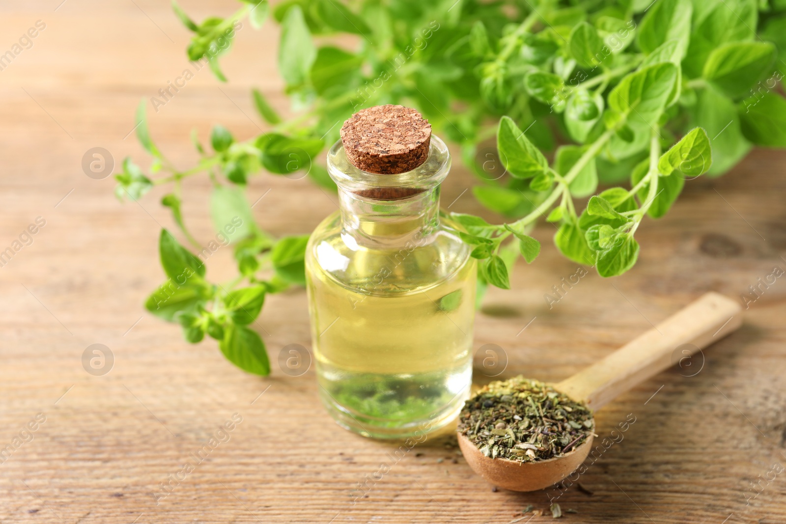 Photo of Essential oil in bottle, spoon with dry herb and oregano twigs on wooden table, closeup