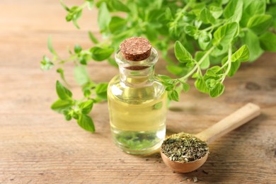 Photo of Essential oil in bottle, spoon with dry herb and oregano twigs on wooden table, closeup