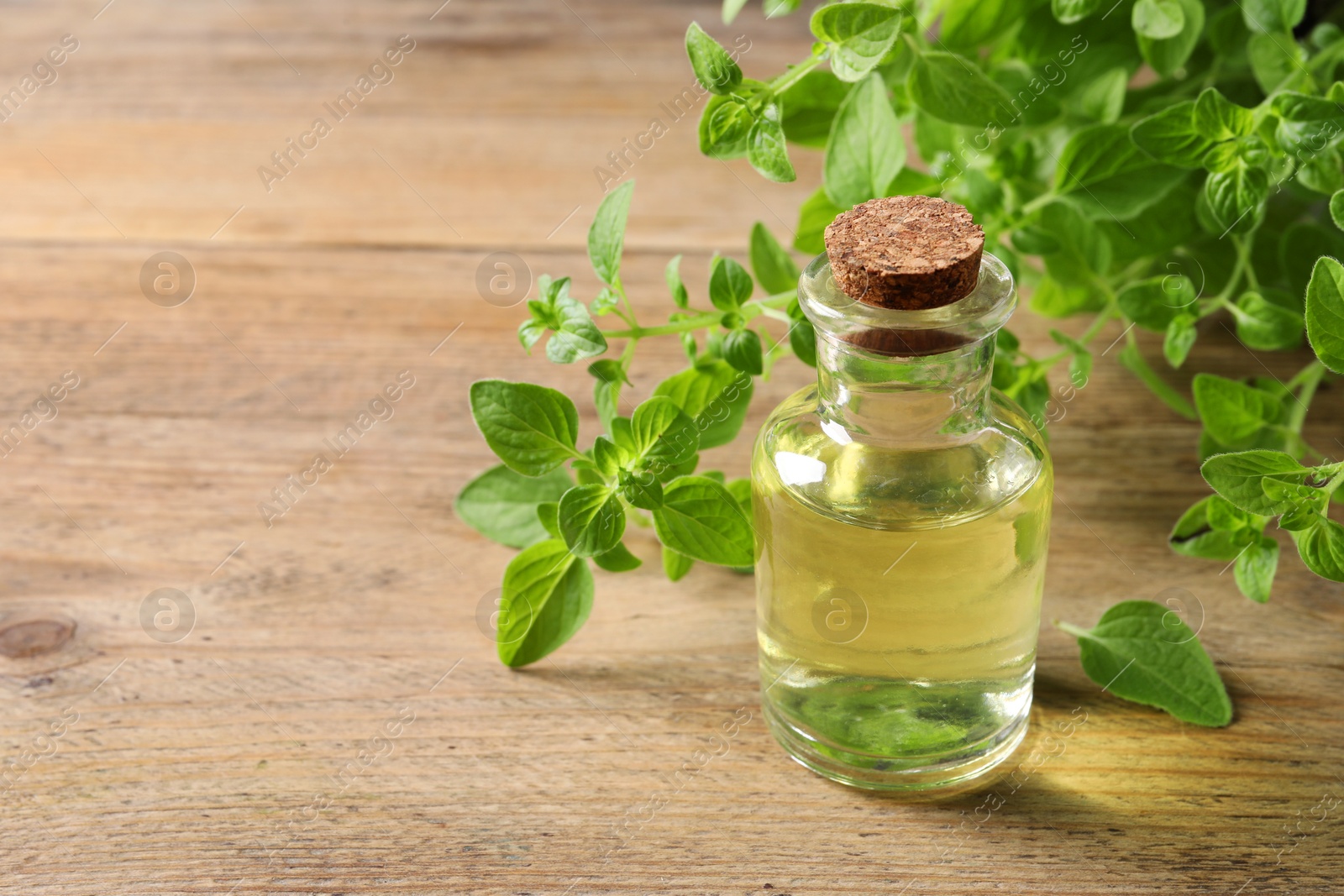 Photo of Essential oil in bottle and oregano twigs on wooden table, closeup. Space for text