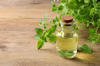 Photo of Essential oil in bottle and oregano twigs on wooden table, closeup. Space for text