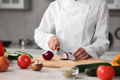 Professional chef cutting onion at table in kitchen, closeup