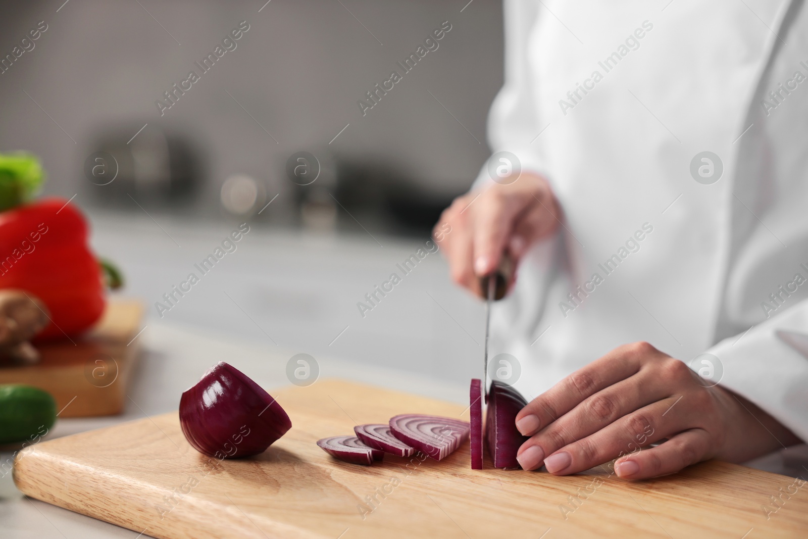 Photo of Professional chef cutting onion at table in kitchen, closeup