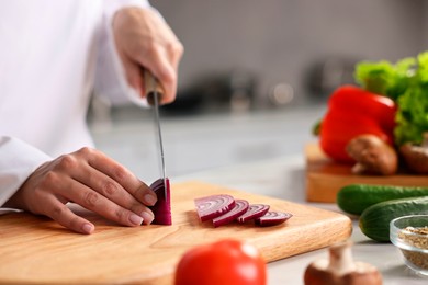 Photo of Professional chef cutting onion at table in kitchen, closeup