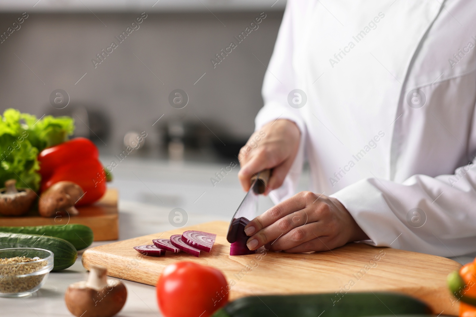 Photo of Professional chef cutting onion at table in kitchen, closeup