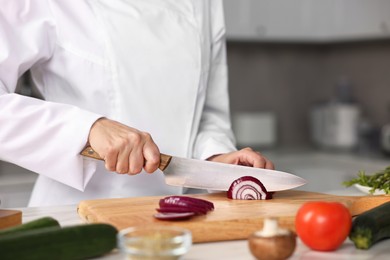 Photo of Professional chef cutting onion at table in kitchen, closeup