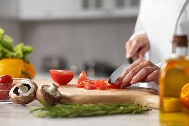 Professional chef cutting tomato at table in kitchen, closeup