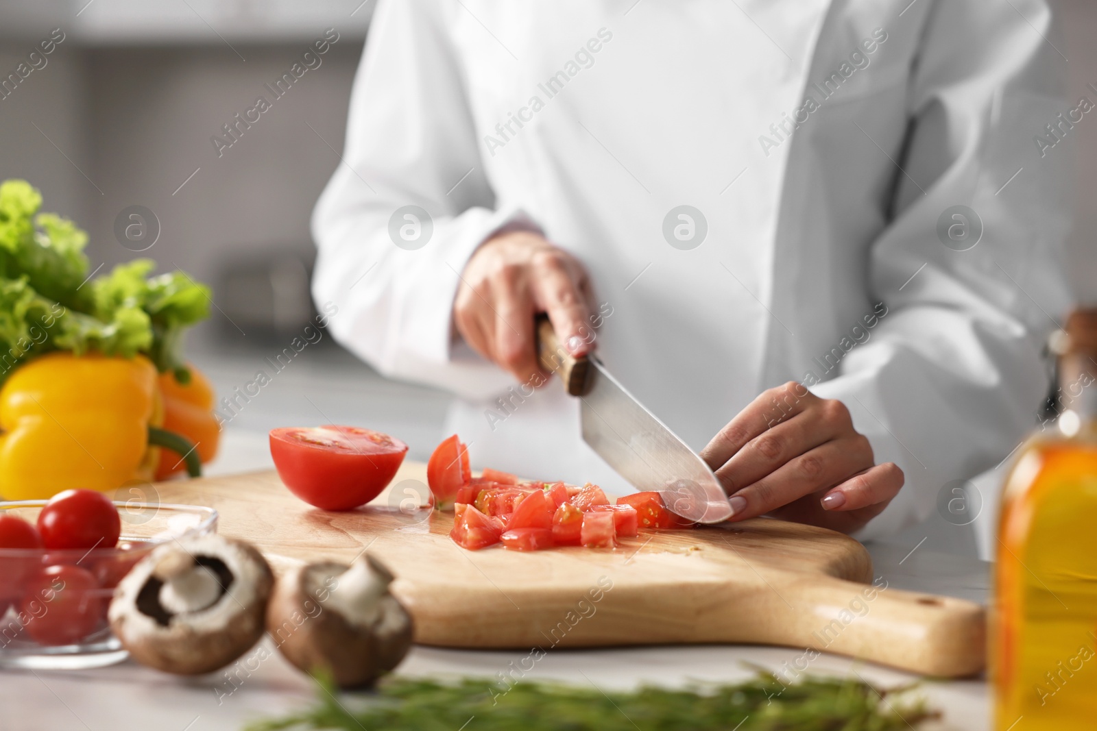 Photo of Professional chef cutting tomato at table in kitchen, closeup