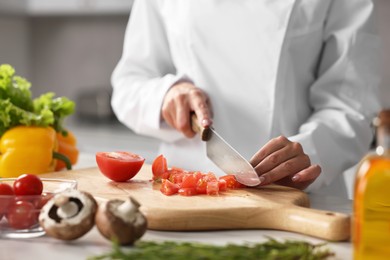 Photo of Professional chef cutting tomato at table in kitchen, closeup