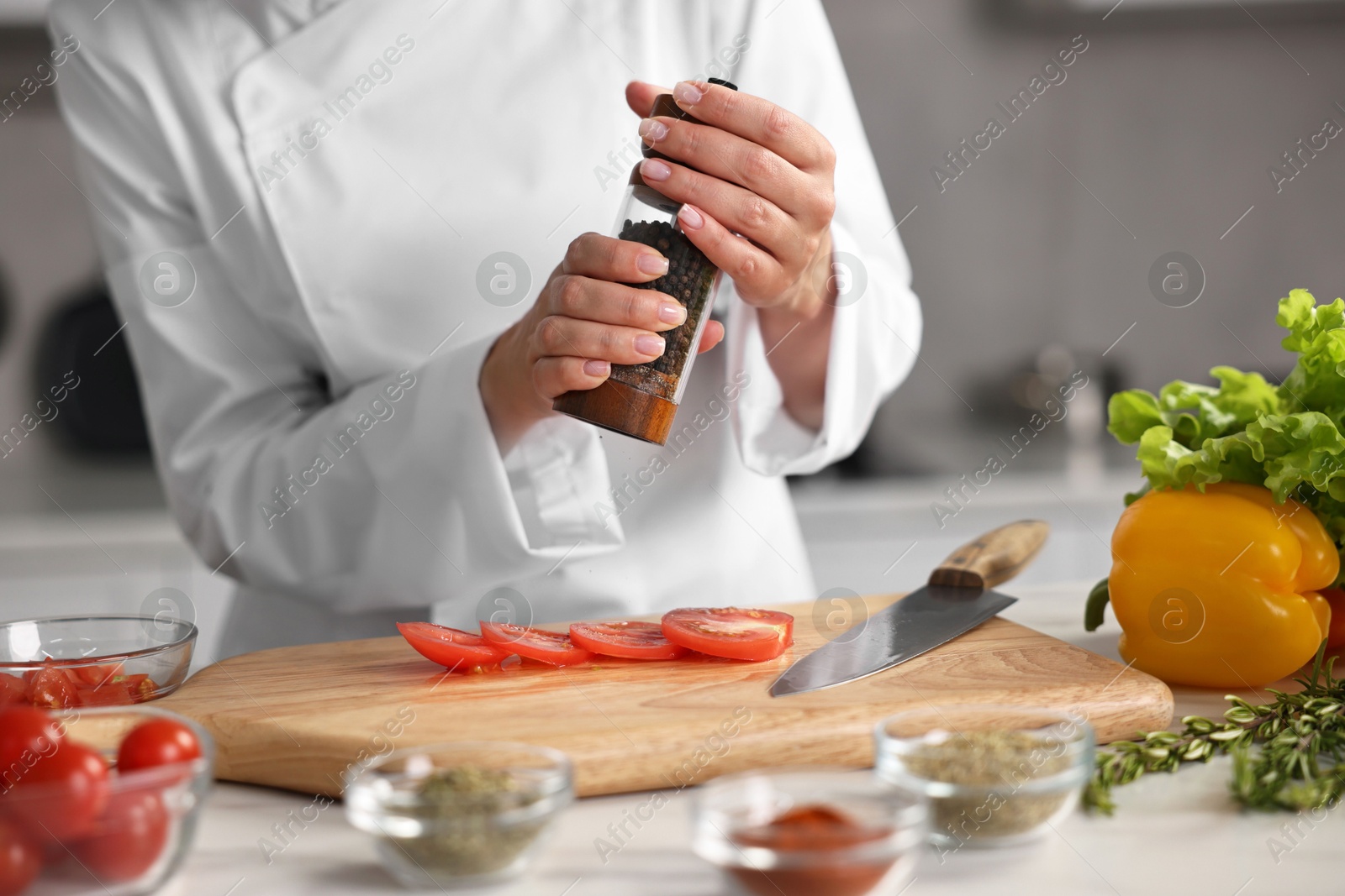 Photo of Professional chef seasoning tomatoes at table in kitchen, closeup