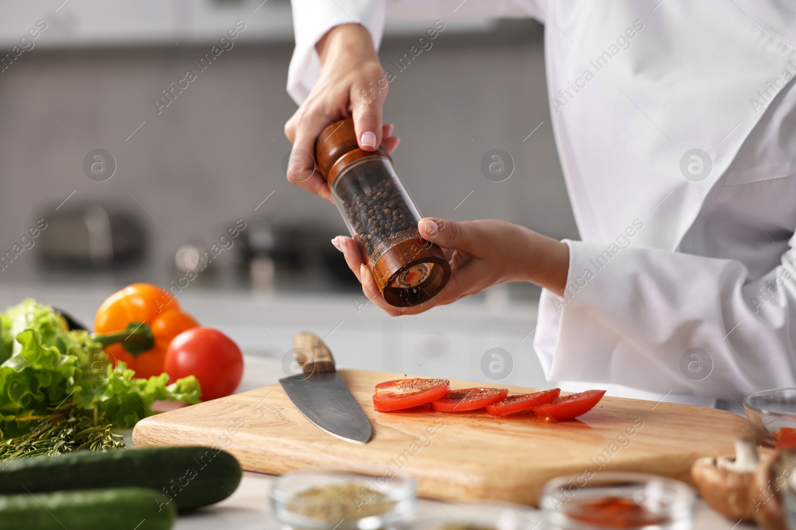 Photo of Professional chef seasoning tomatoes at table in kitchen, closeup