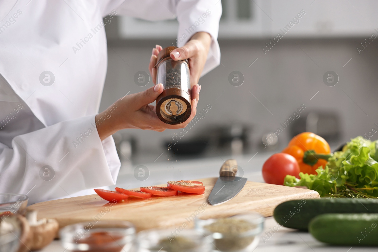 Photo of Professional chef seasoning tomatoes at table in kitchen, closeup