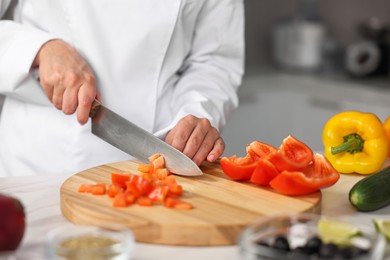 Professional chef cutting pepper at table in kitchen, closeup