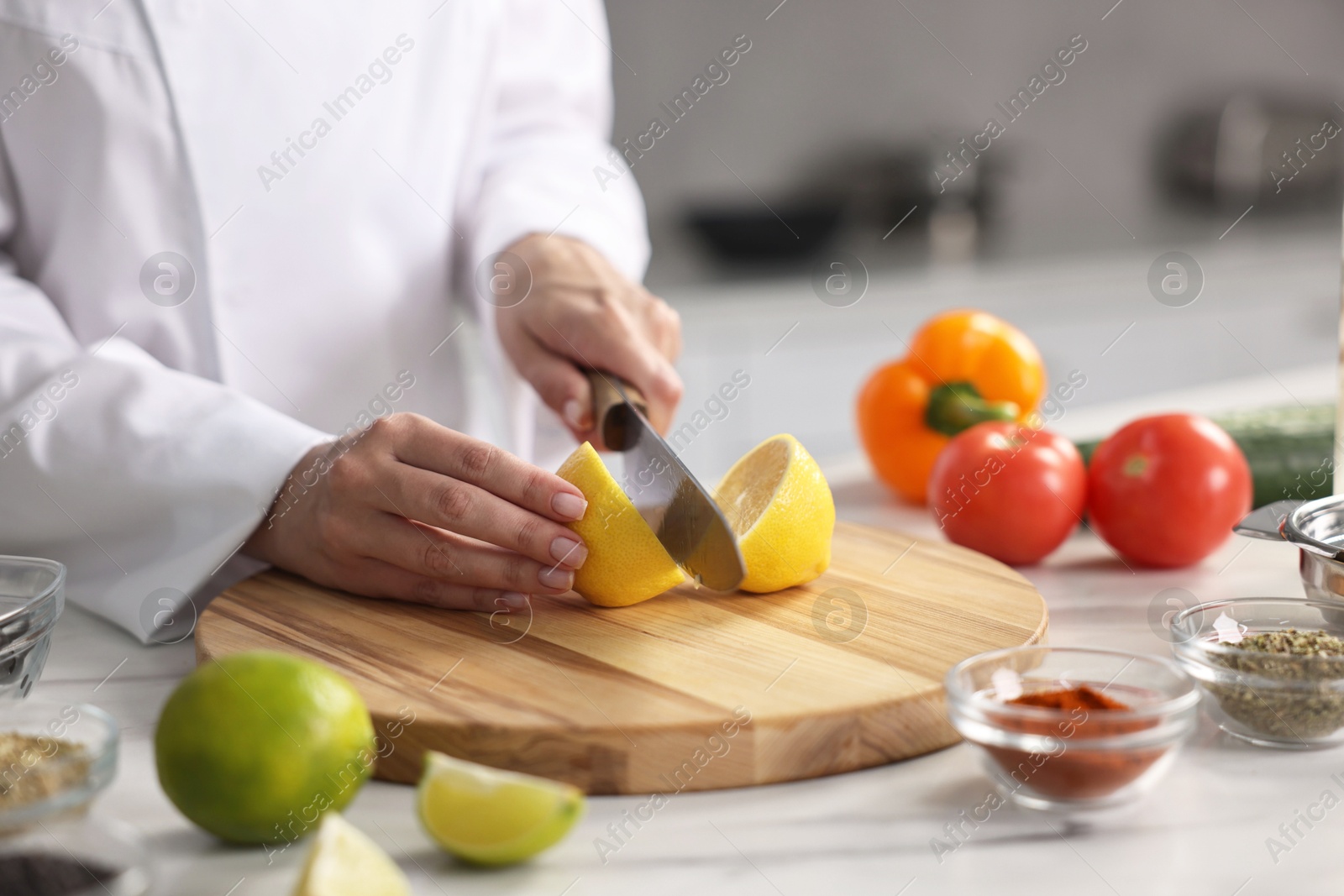 Photo of Professional chef cutting lemon at table in kitchen, closeup