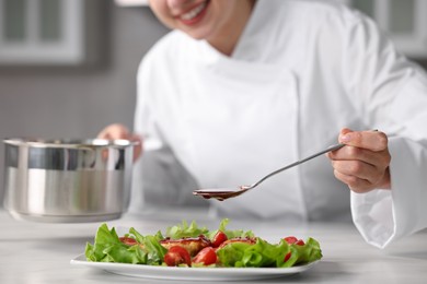 Professional chef adding sauce to dish with baked chicken at white marble table in kitchen, closeup