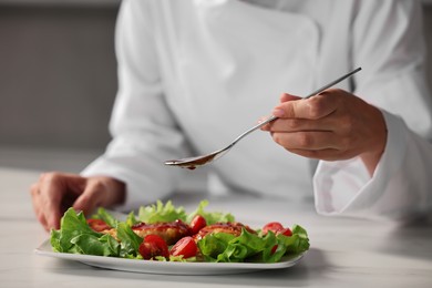 Professional chef adding sauce to dish with baked chicken at white marble table in kitchen, closeup