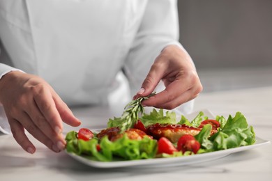 Photo of Professional chef decorating dish with rosemary at table in kitchen