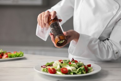 Professional chef adding pepper to delicious salad at white marble table in kitchen, closeup