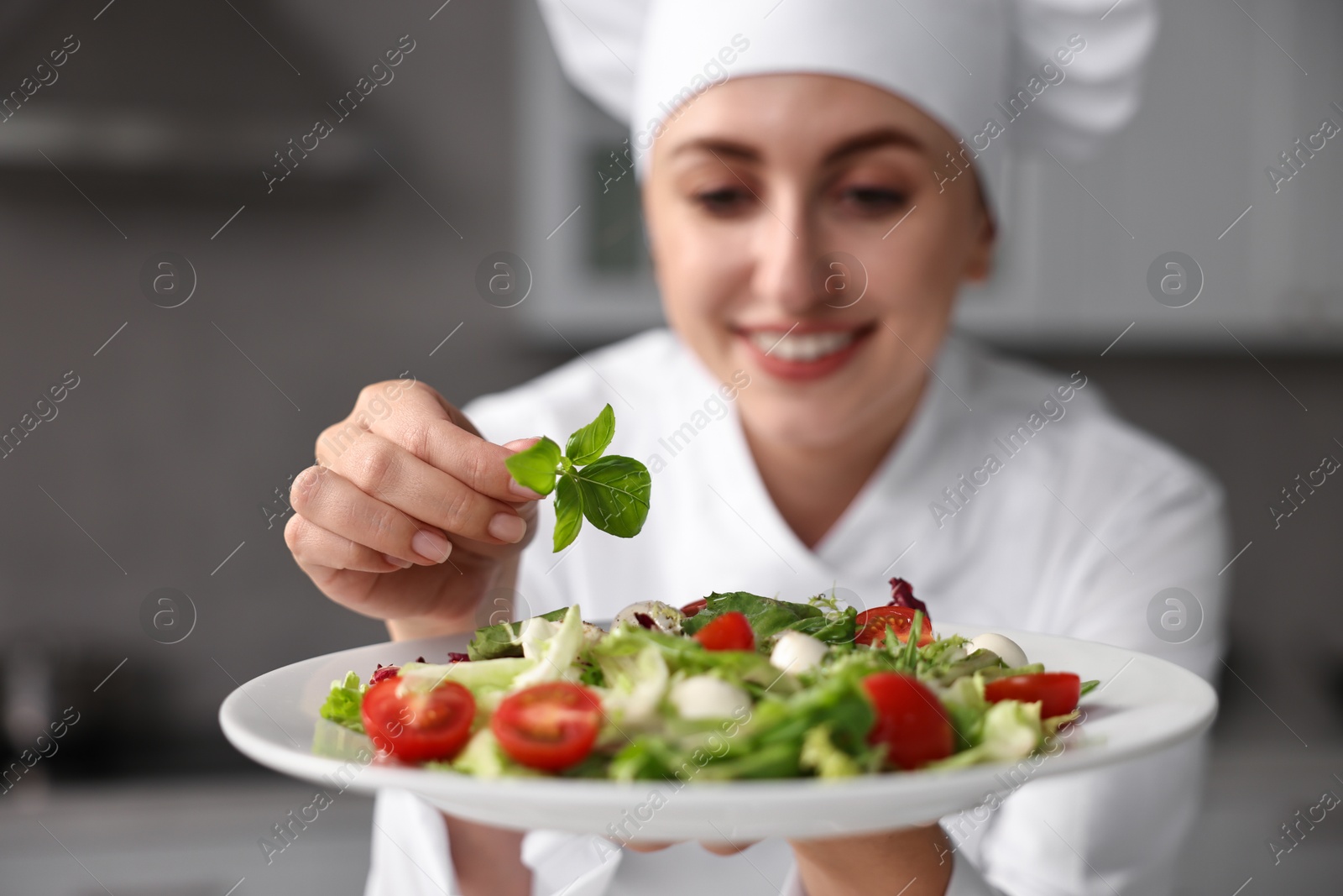 Photo of Professional chef decorating delicious salad with basil in kitchen, selective focus