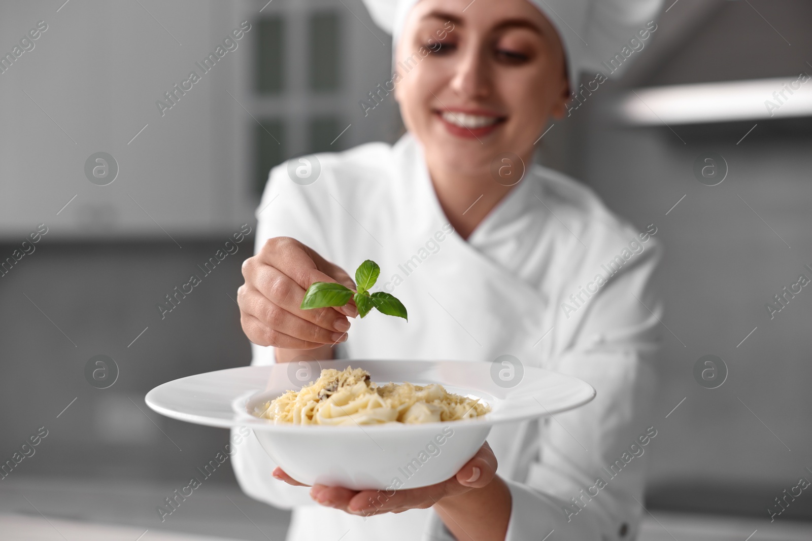 Photo of Professional chef decorating delicious pasta with basil in kitchen, selective focus