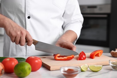 Photo of Professional chef cutting bell pepper at white marble table in kitchen, closeup