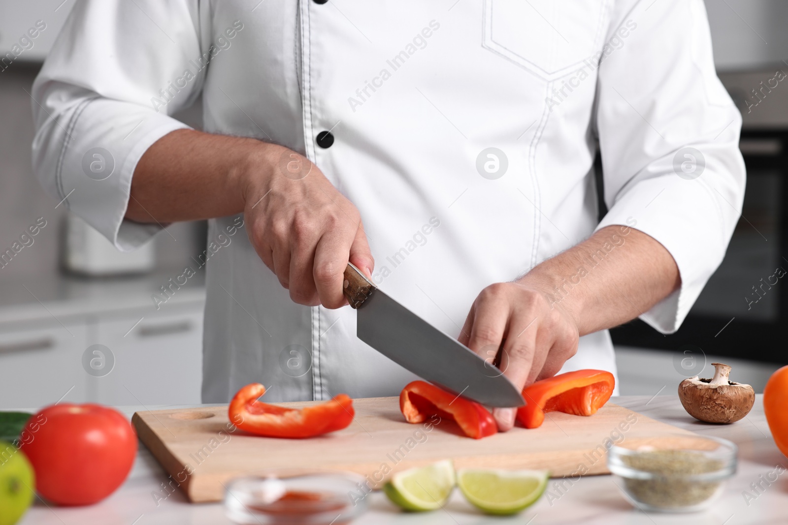 Photo of Professional chef cutting bell pepper at table in kitchen, closeup