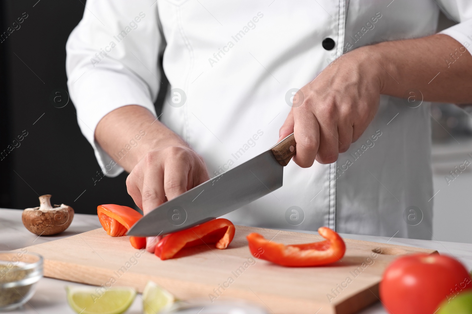 Photo of Professional chef cutting bell pepper at table in kitchen, closeup