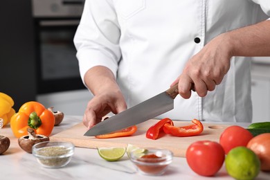 Photo of Professional chef cutting bell pepper at white marble table in kitchen, closeup