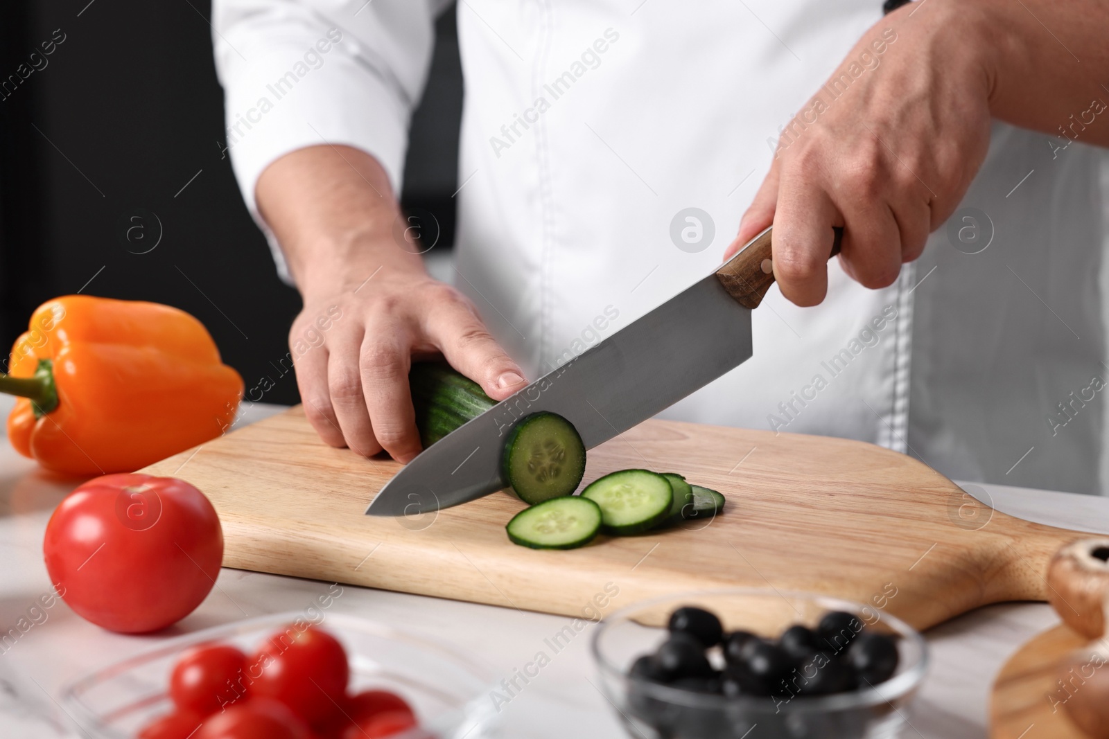 Photo of Professional chef cutting cucumber at table in kitchen, closeup