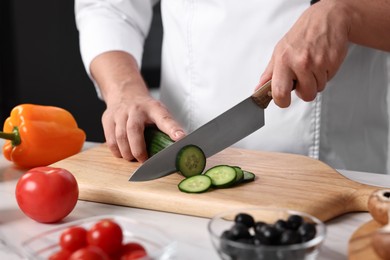 Professional chef cutting cucumber at table in kitchen, closeup