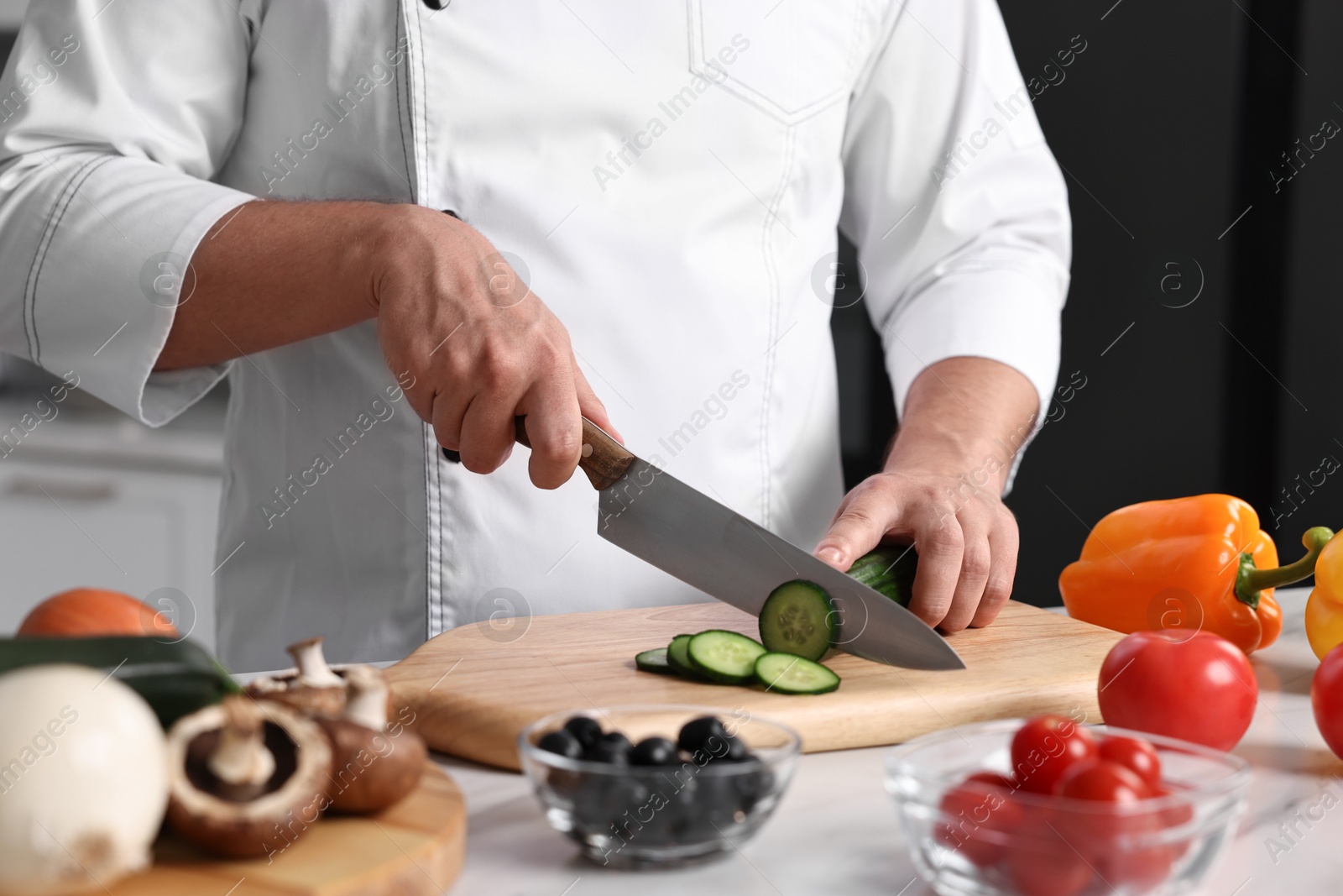 Photo of Professional chef cutting cucumber at table in kitchen, closeup