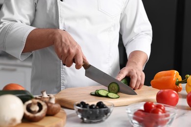 Professional chef cutting cucumber at table in kitchen, closeup