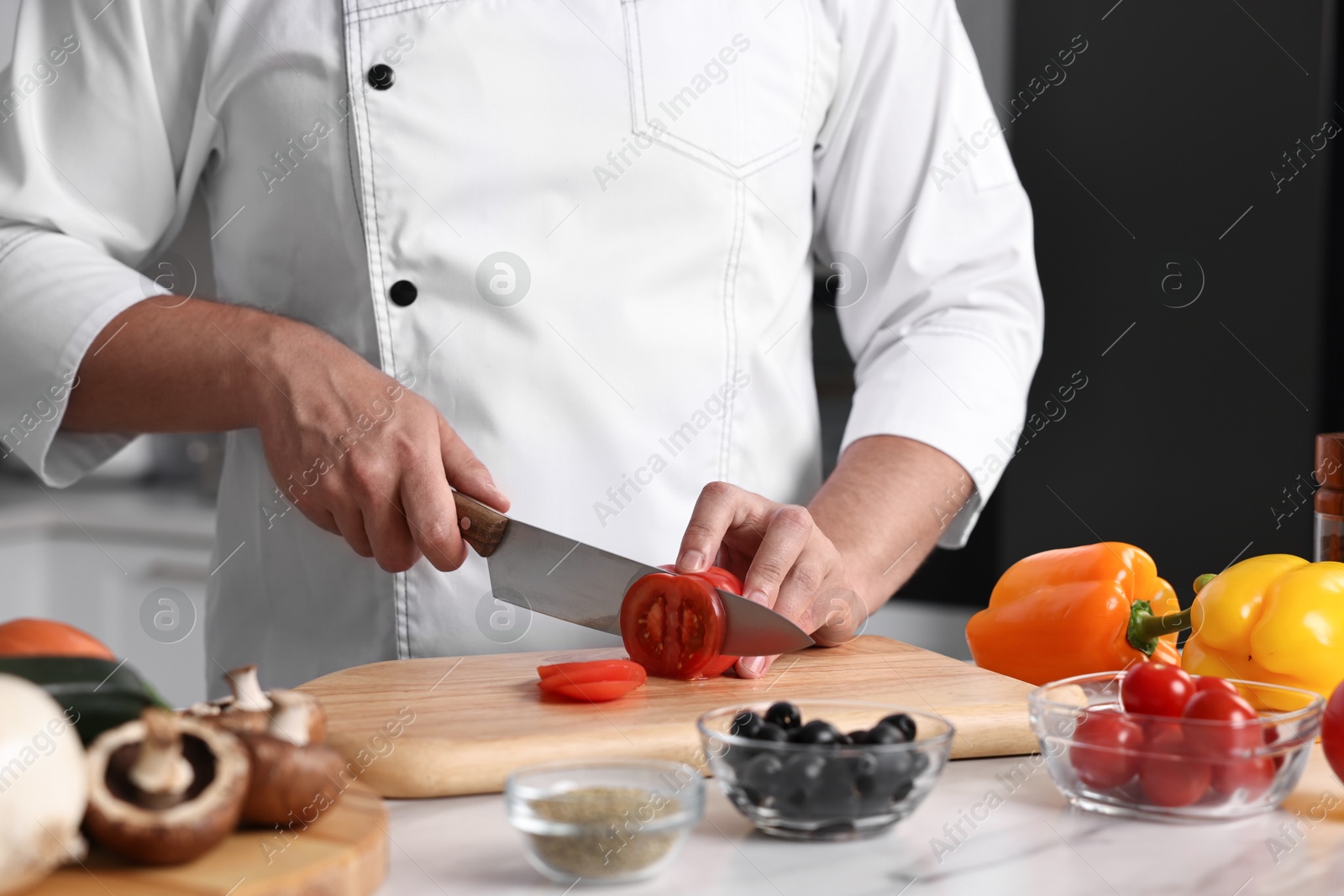 Photo of Professional chef cutting tomato at table in kitchen, closeup