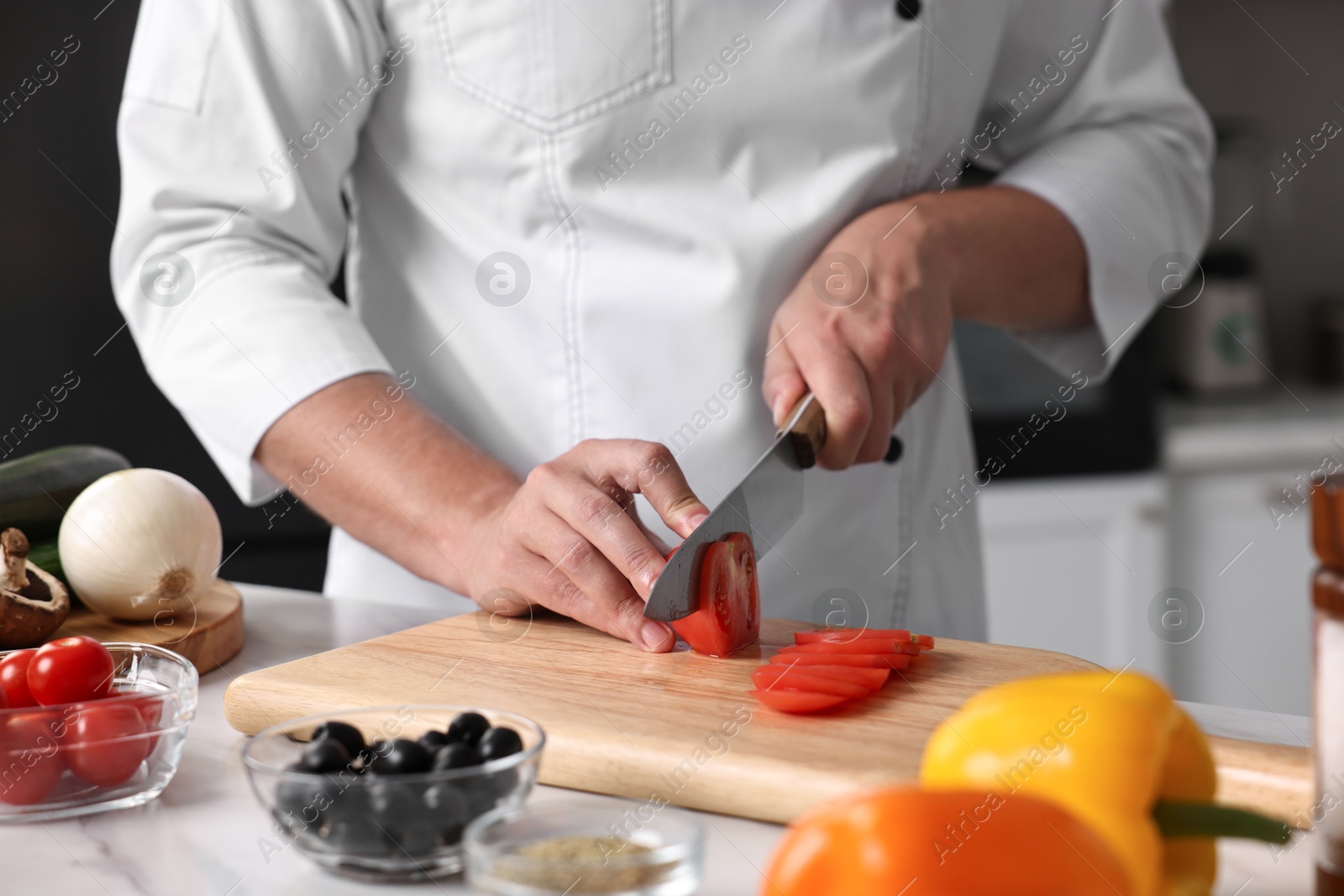 Photo of Professional chef cutting tomato at table in kitchen, closeup