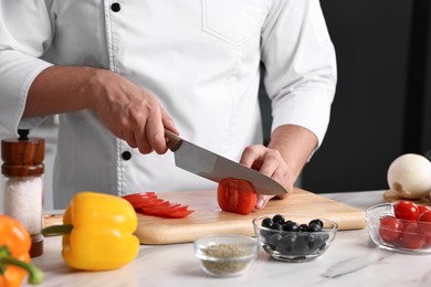 Professional chef cutting tomato at table in kitchen, closeup