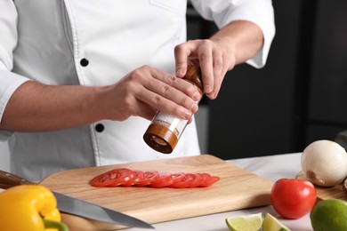 Photo of Professional chef adding salt to tomato at table in kitchen, closeup