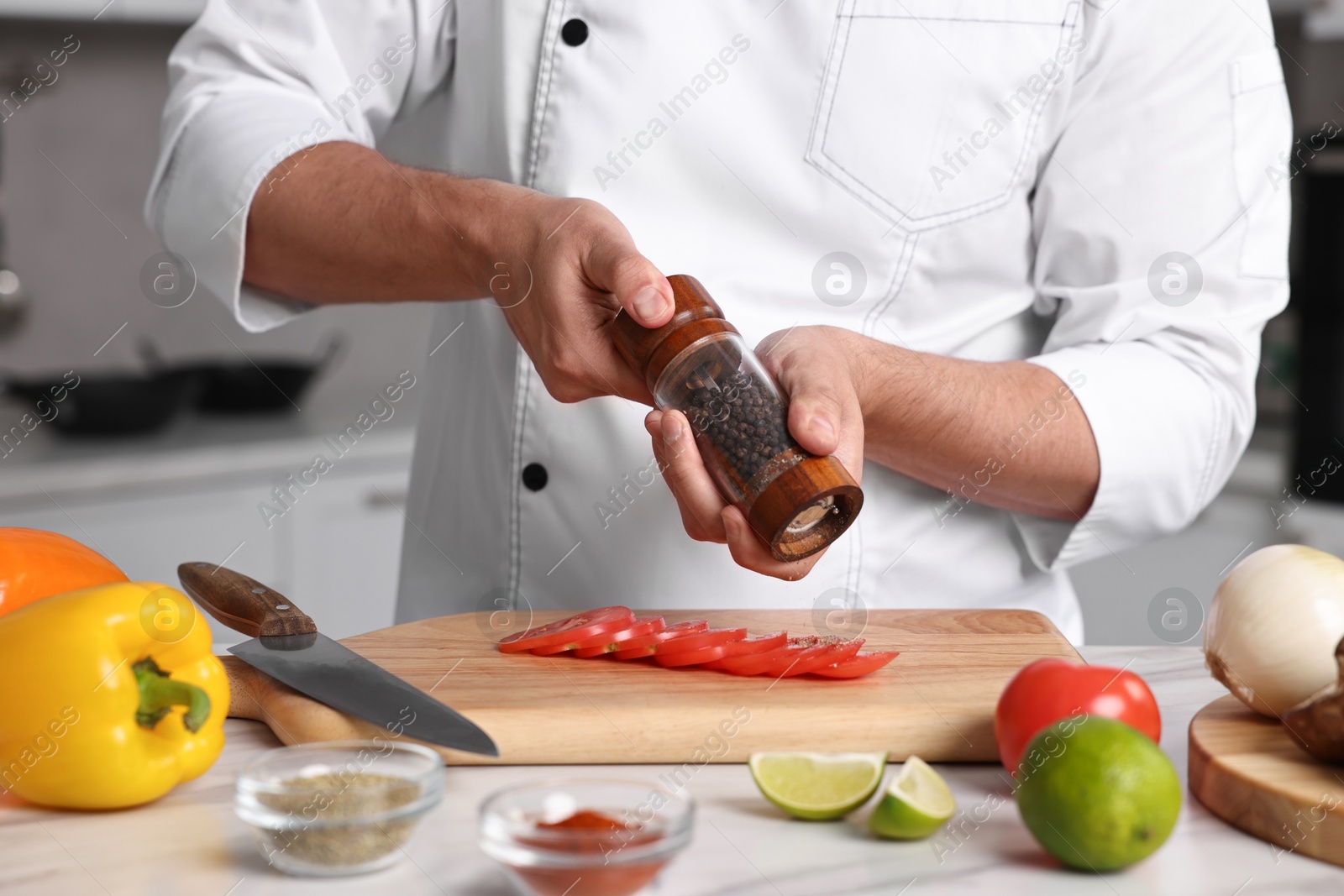 Photo of Professional chef adding pepper to tomato at table in kitchen, closeup