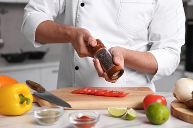 Professional chef adding pepper to tomato at table in kitchen, closeup