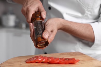 Photo of Professional chef adding pepper to tomato in kitchen, closeup