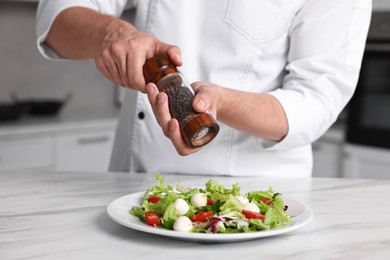 Professional chef adding pepper to delicious salad at white marble table in kitchen, closeup