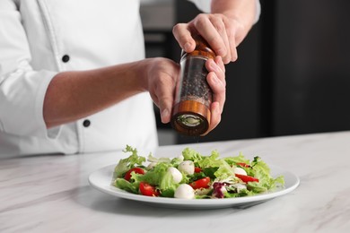 Professional chef adding pepper to delicious salad at white marble table in kitchen, closeup