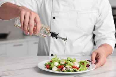 Photo of Professional chef pouring oil onto delicious salad at white marble table in kitchen, closeup