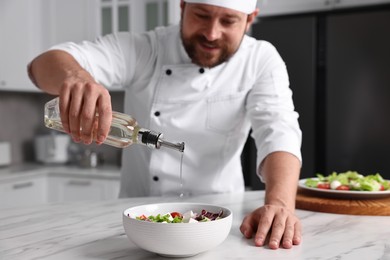 Professional chef pouring oil onto delicious salad at white marble table in kitchen, selective focus