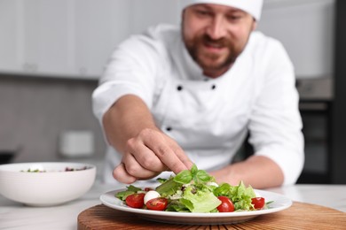 Photo of Professional chef decorating delicious salad with basil at table in kitchen, selective focus