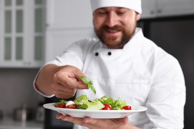 Professional chef decorating delicious salad with basil in kitchen, selective focus