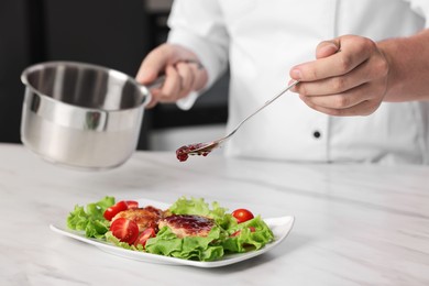 Photo of Professional chef pouring sauce onto delicious dish at white marble table in kitchen, closeup