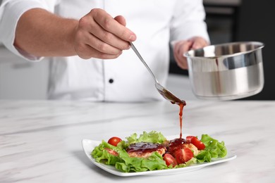 Professional chef pouring sauce onto delicious dish at white marble table in kitchen, closeup