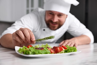 Professional chef decorating delicious dish with rosemary at white marble table in kitchen, selective focus